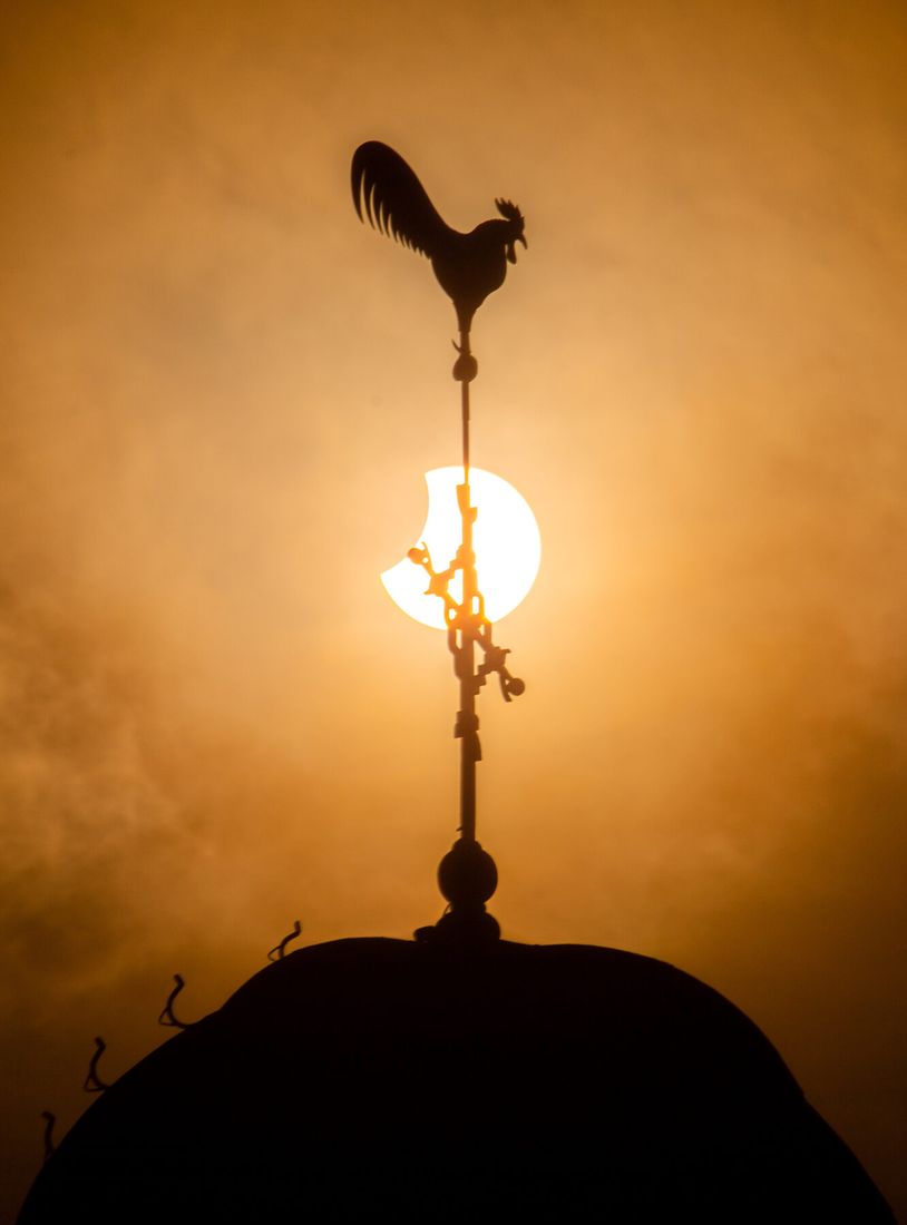 Kerktoren met windhaan tegen de gedeeltelijk verduisterde zon